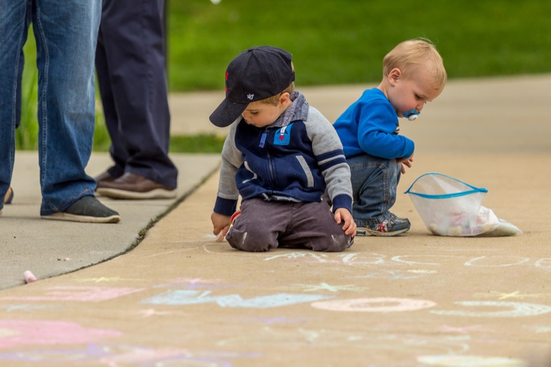 Toddler boys drawing on concrete with chalk