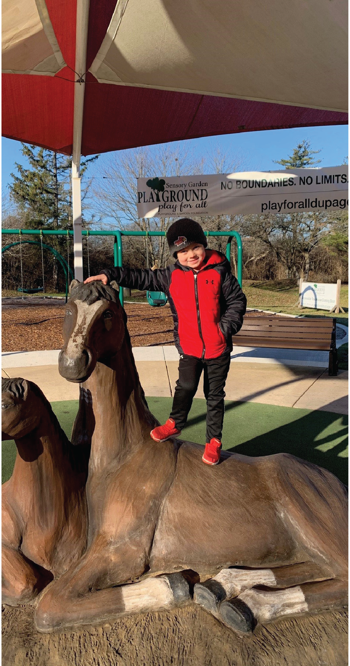 Karl Berland's grandson standing on top of a plastic horse at the Sensory Garden Playground